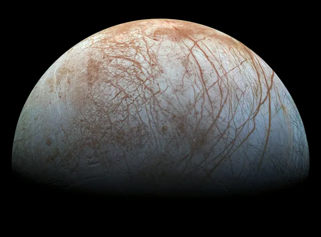Europa, a pale moon crossed by reddish cracks, in a mosaic from the Galileo spacecraft