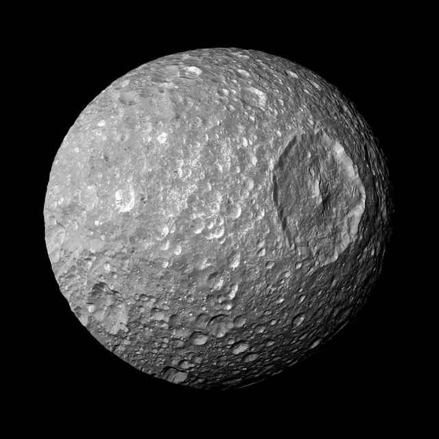 Mimas, a grey moon full of craters with the huge crater Herschel on one side, photographed by Cassini